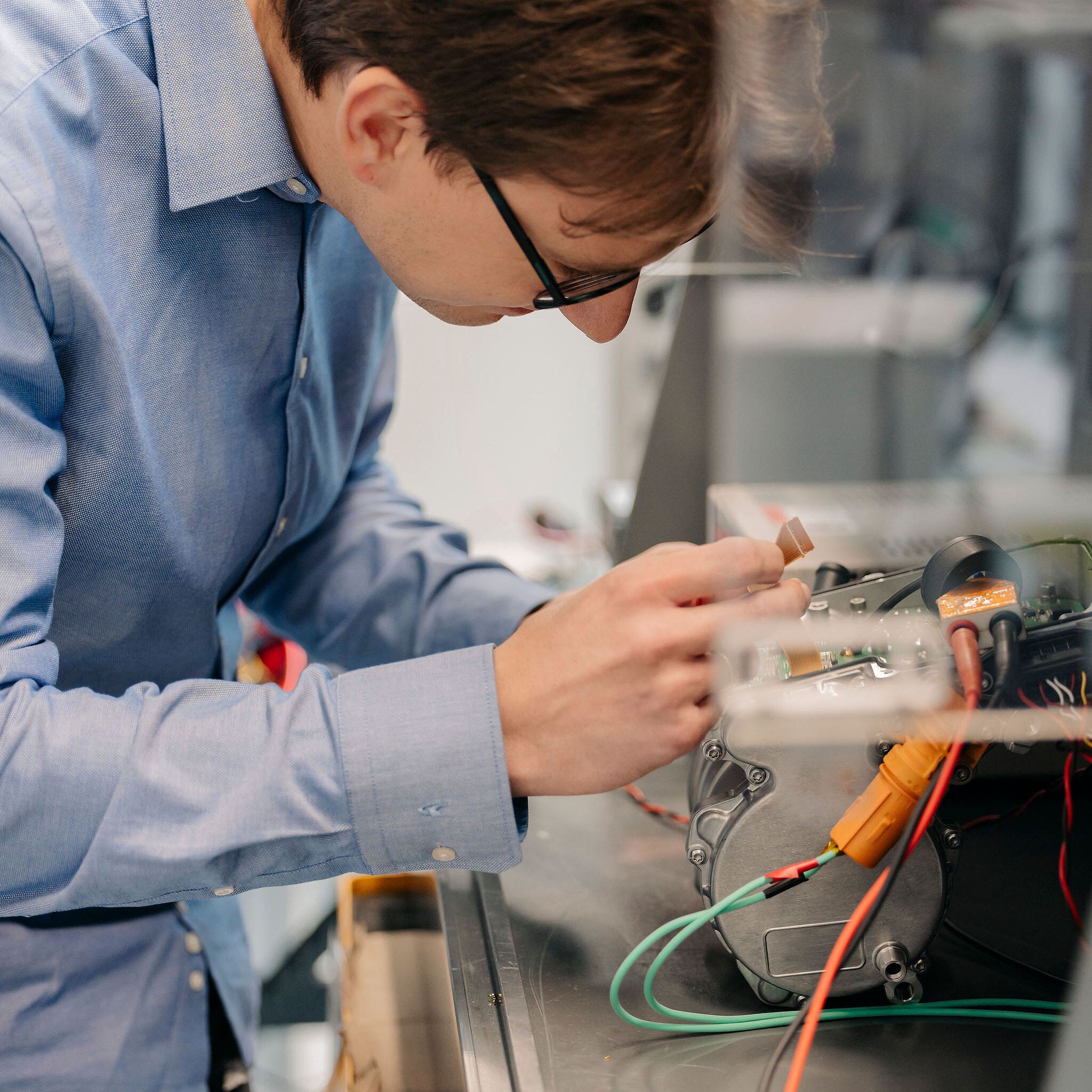 Silver Atena engineer examining an electronic assembly with a metal housing and connected cables in the development laboratory.