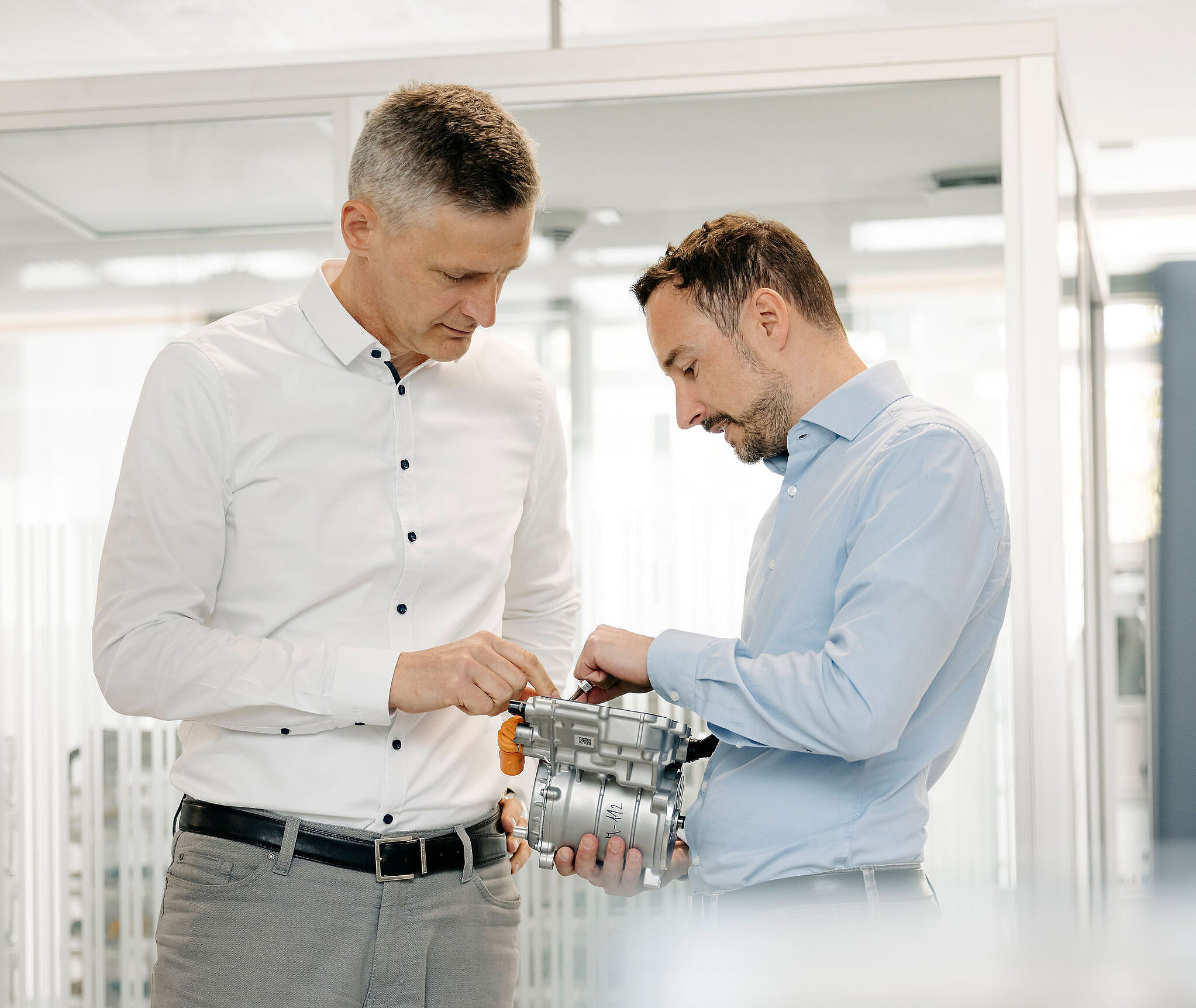Two Silver Atena engineers jointly examining an electronic drive unit with a metal housing and connectors.