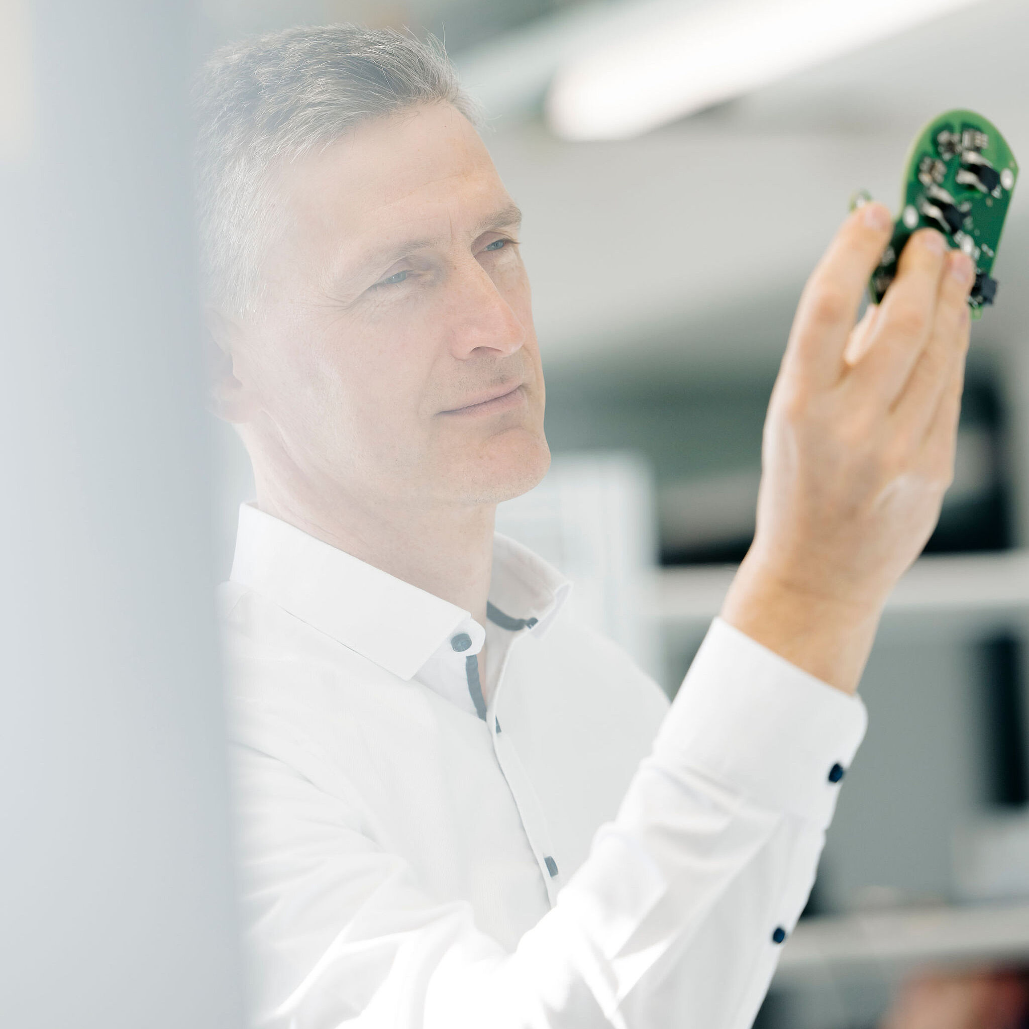 Silver Atena employee visually inspecting an assembled printed circuit board (PCB) as part of a quality inspection.