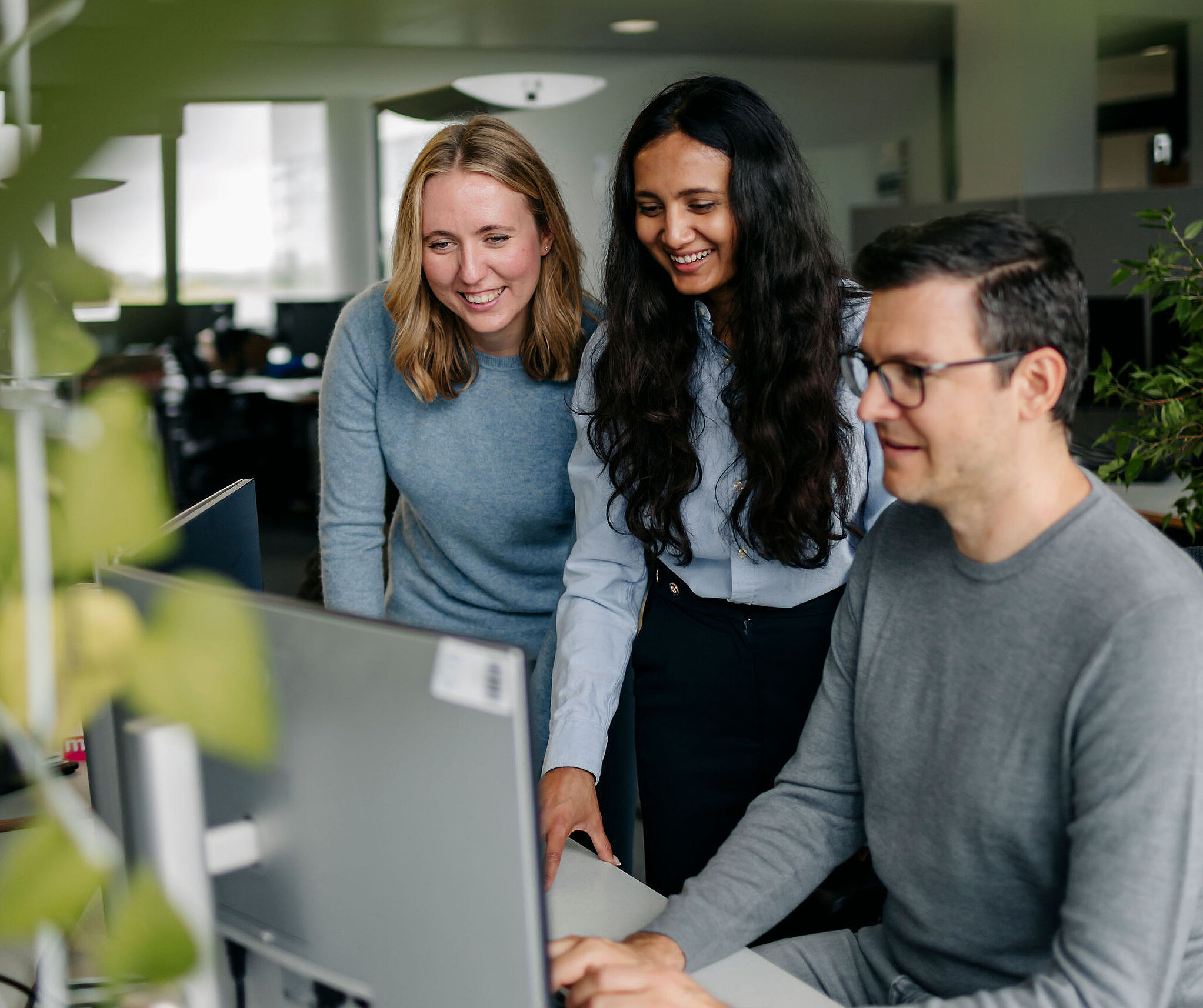 Three Silver Atena employees working together at a computer workstation and discussing technical project details.