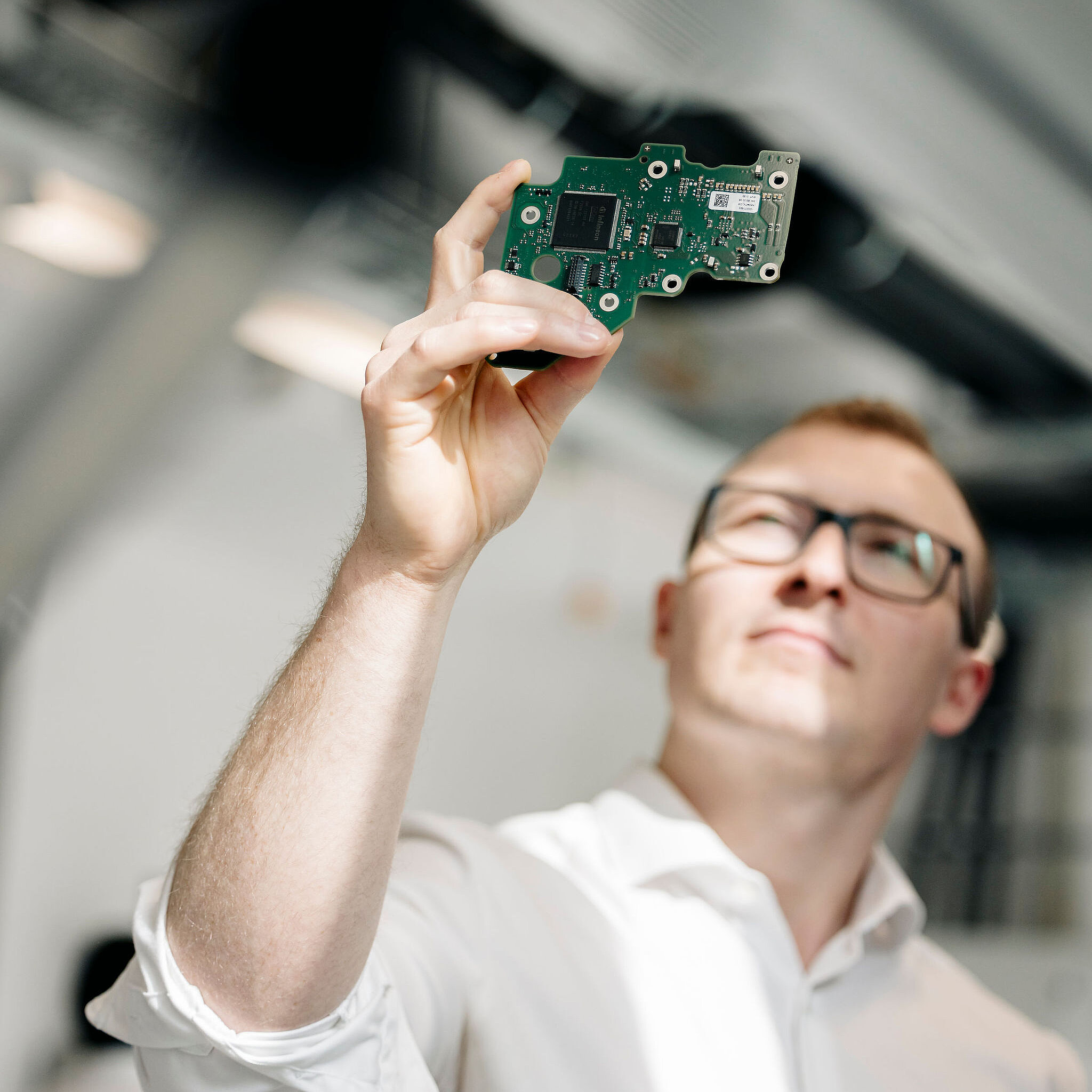 Silver Atena engineer holding an assembled printed circuit board up to the light to visually inspect its electronic components.