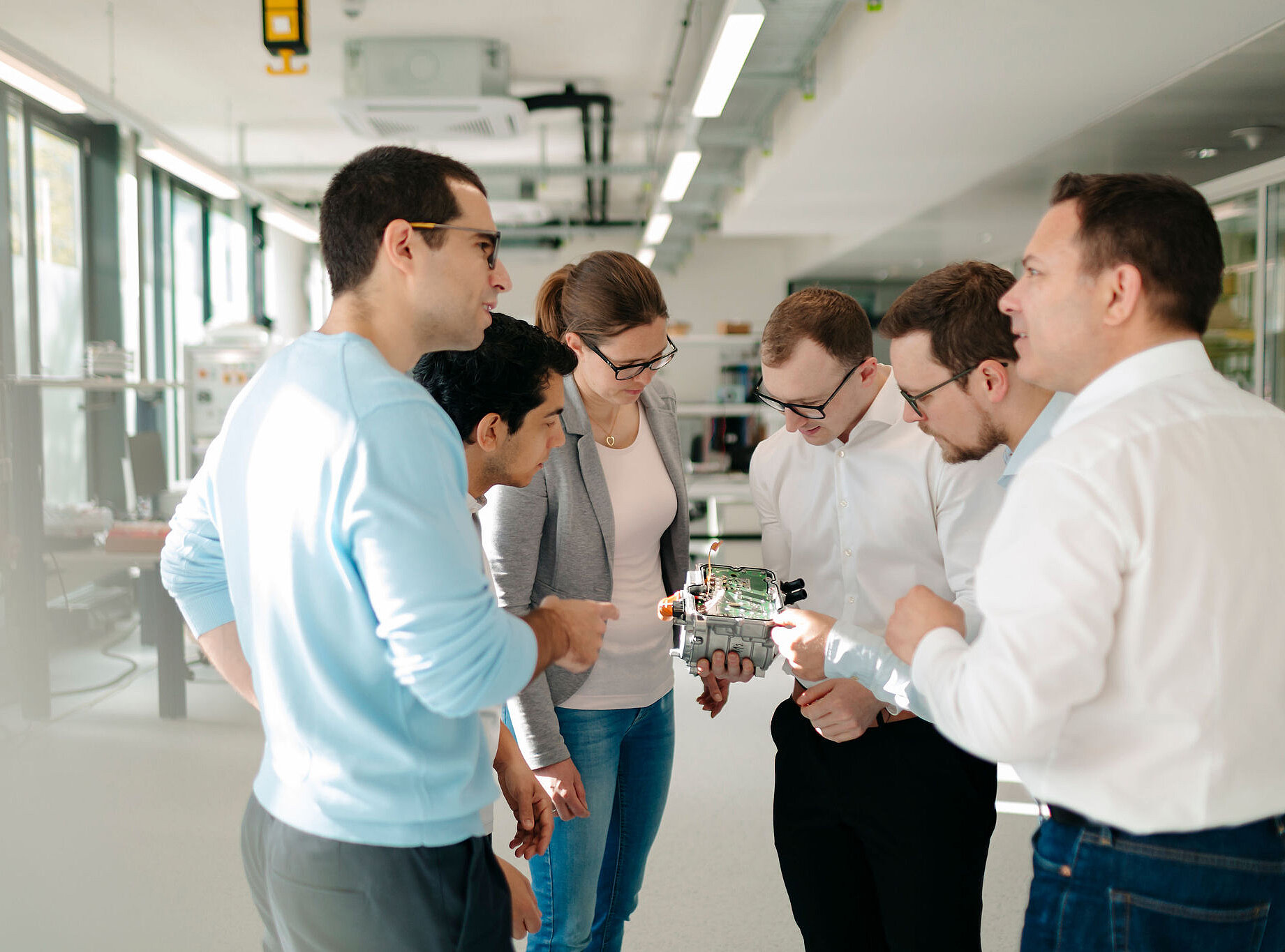 Six Silver Atena employees discussing the integration of a printed circuit board (PCB) into an open electronic control unit housing.