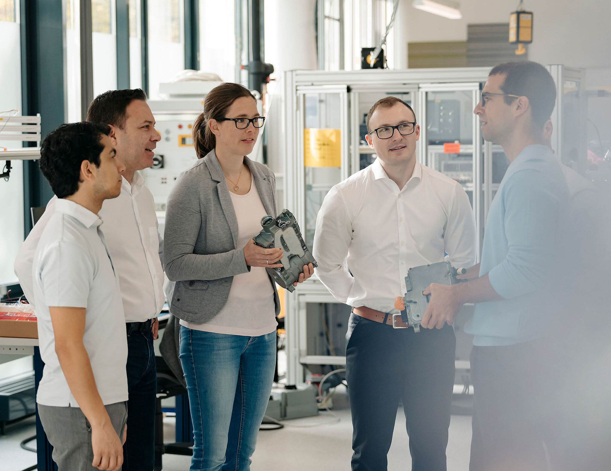 Five Silver Atena employees discussing electronic assemblies and housing components together in the development laboratory.