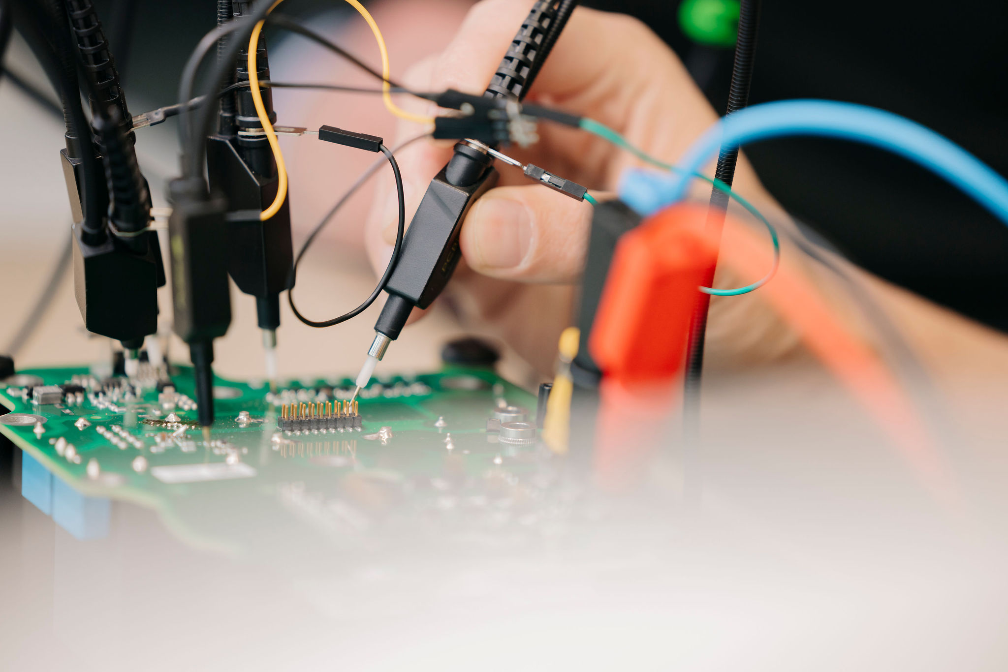 Close-up of a printed circuit board (PCB) undergoing testing with multiple measurement probes and connected test leads