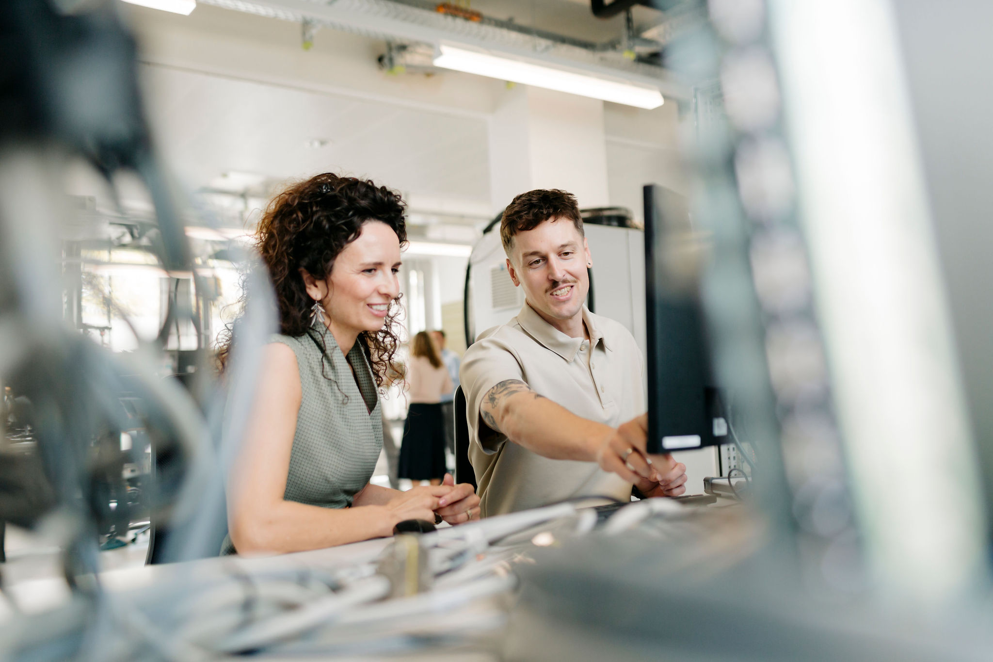 Two Silver Atena employees discussing technical details at a computer workstation in the development laboratory