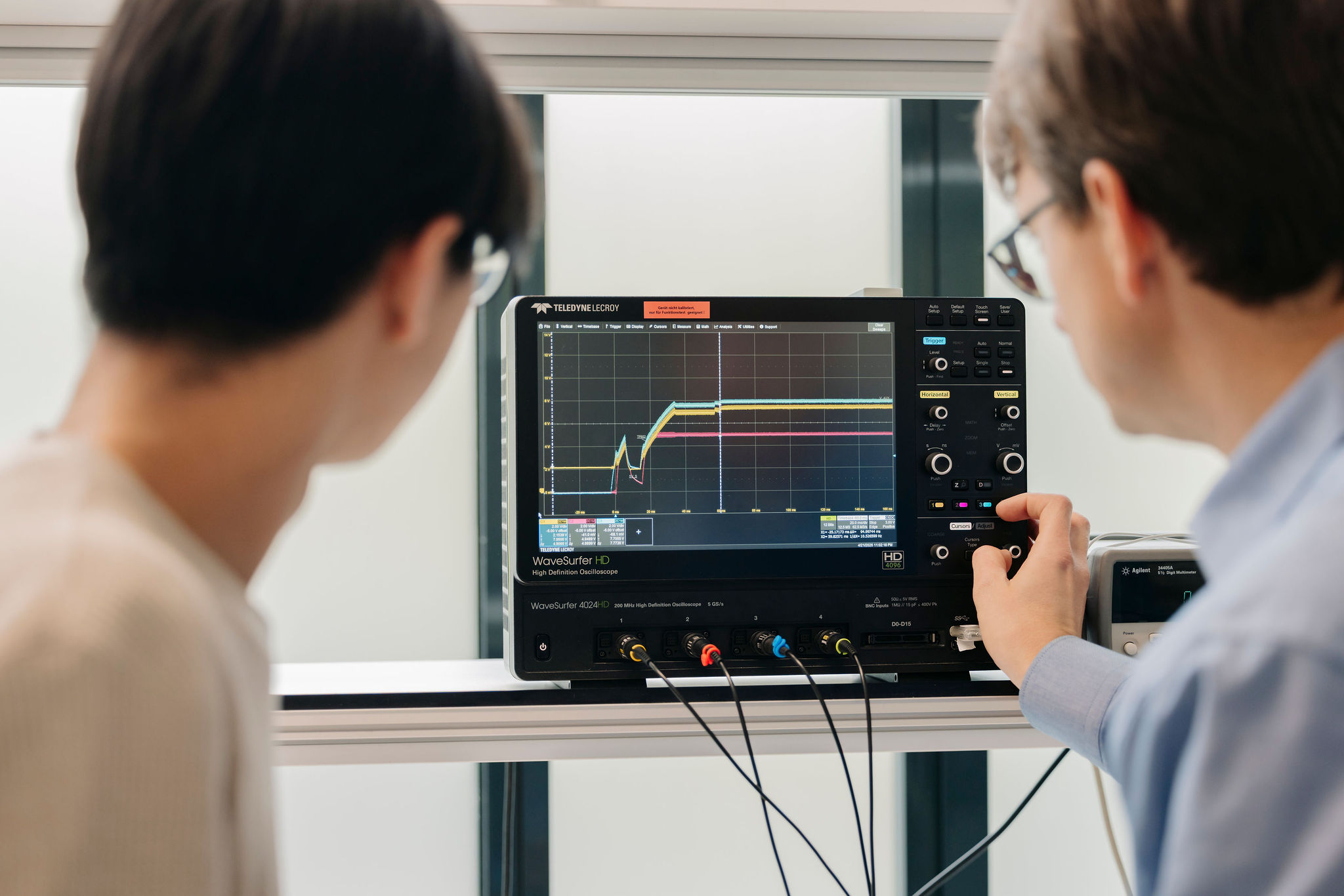 Two engineers analyzing electrical waveforms on an oscilloscope in the electronics laboratory.