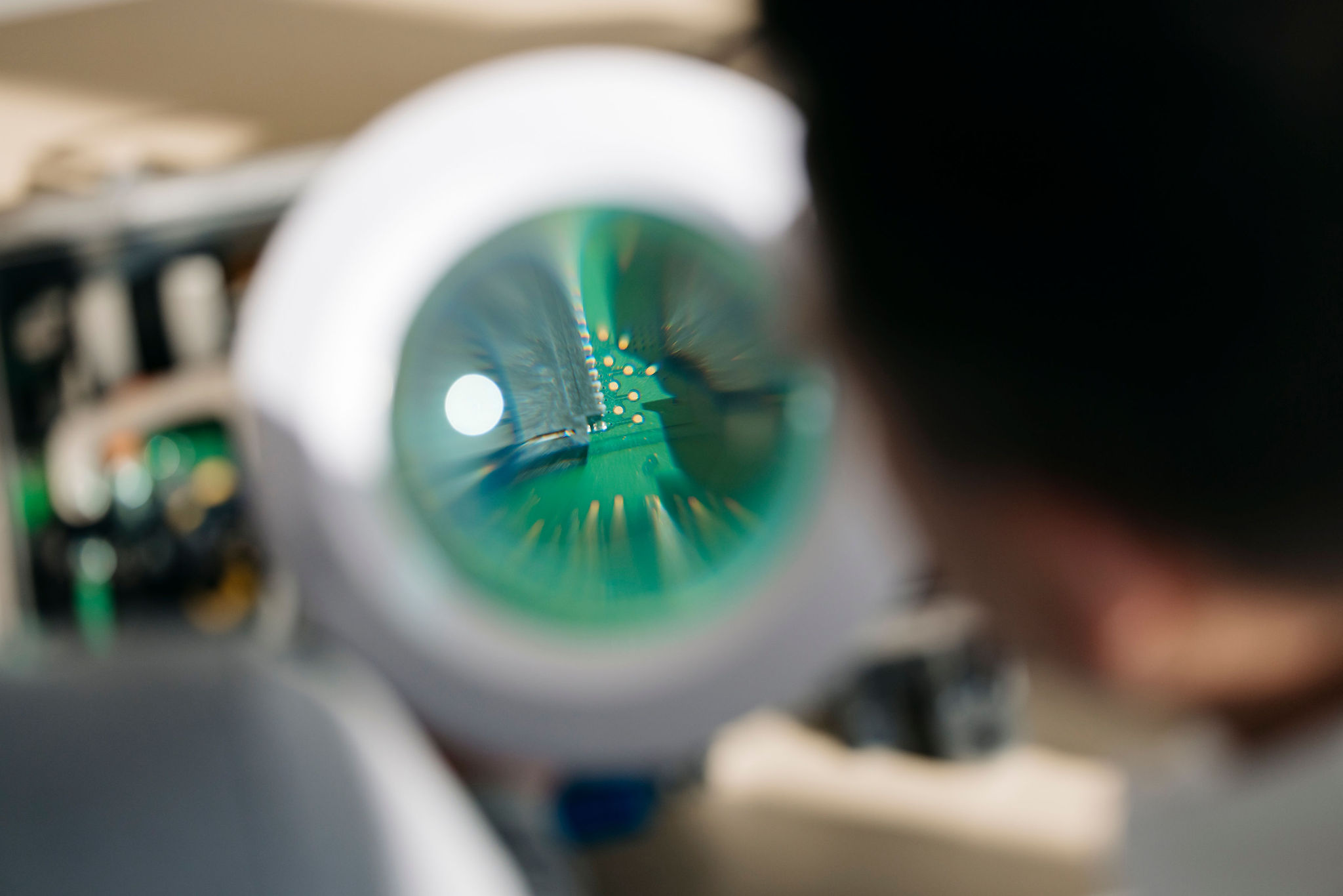 Close-up of a printed circuit board (PCB) viewed through an illuminated magnifying glass to inspect fine circuit traces and electrical contacts.