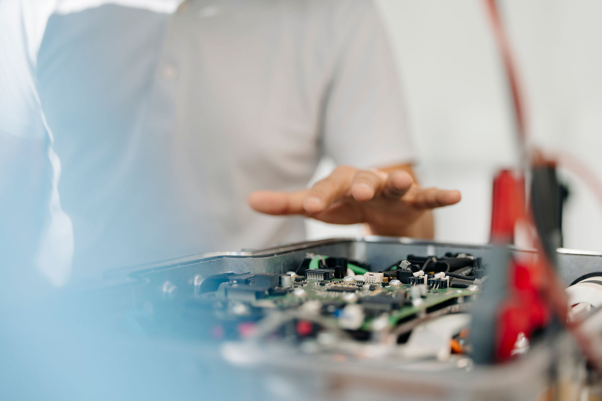 Close-up of an electronic assembly with a printed circuit board inside an open metal housing during a technical discussion.