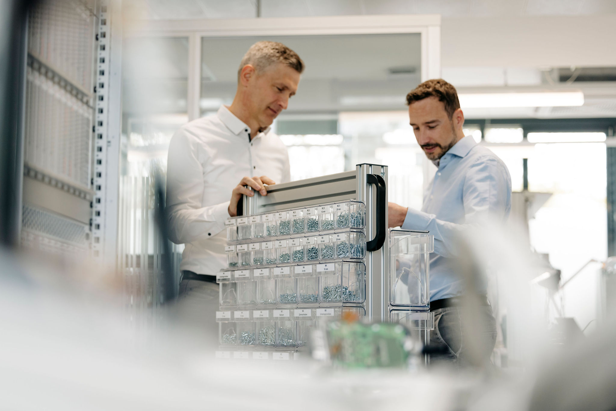 Two Silver Atena employees discussing technical components and assembly materials at a workstation in the development laboratory.