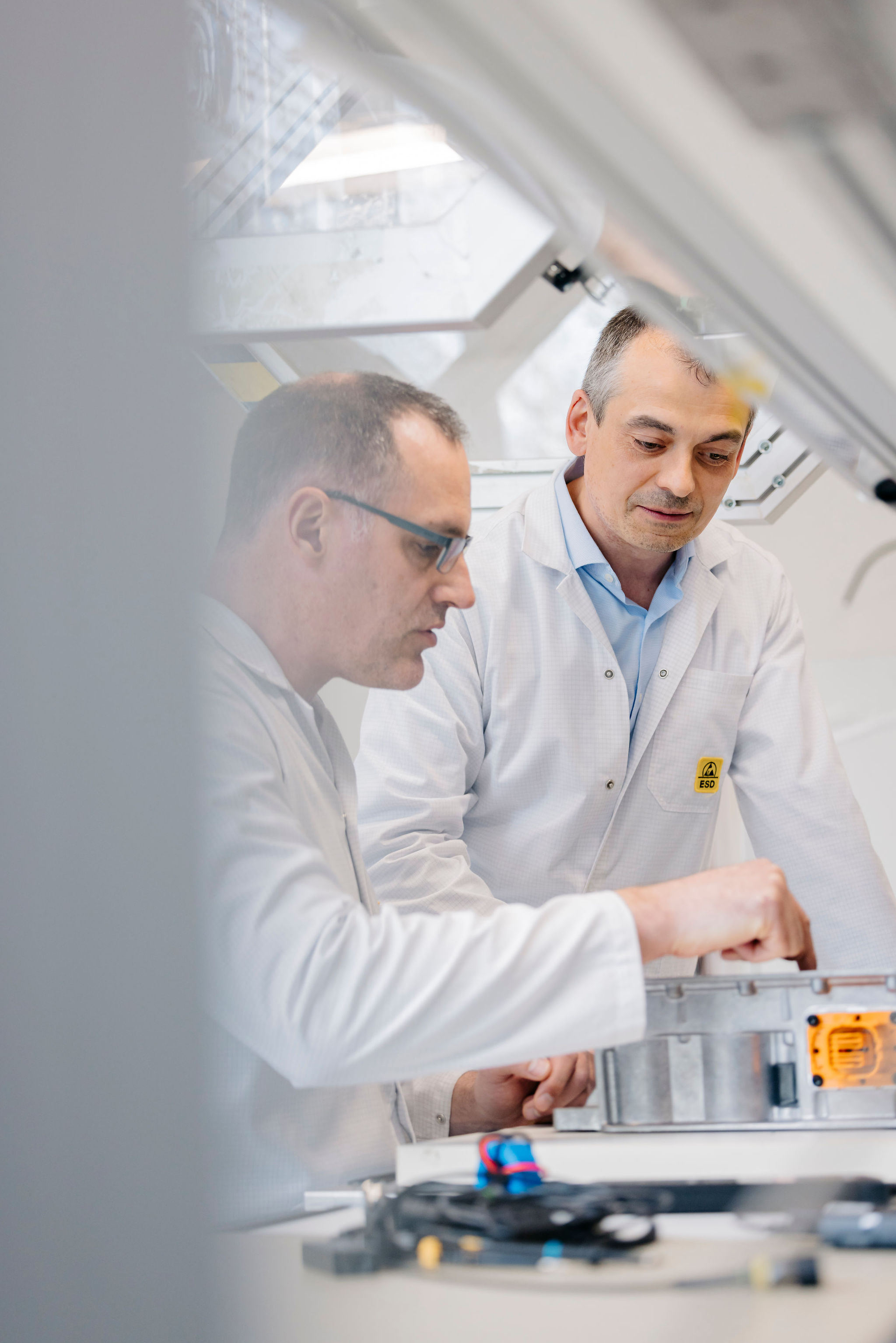 Two Silver Atena employees inspecting an electronic control unit housing at an ESD-protected laboratory workstation.