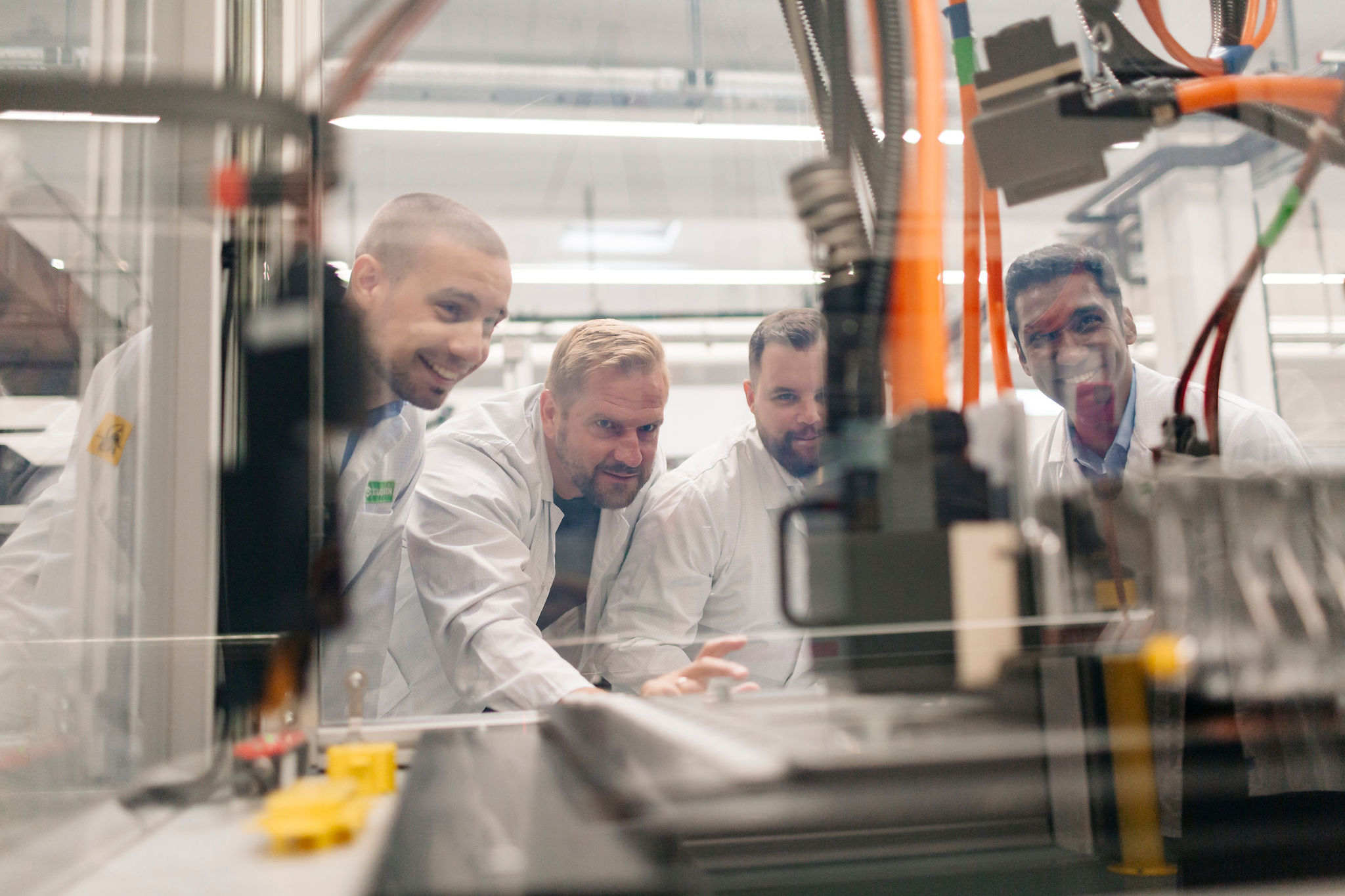 Four Silver Atena employees jointly inspecting an automated production system with electronic assemblies.