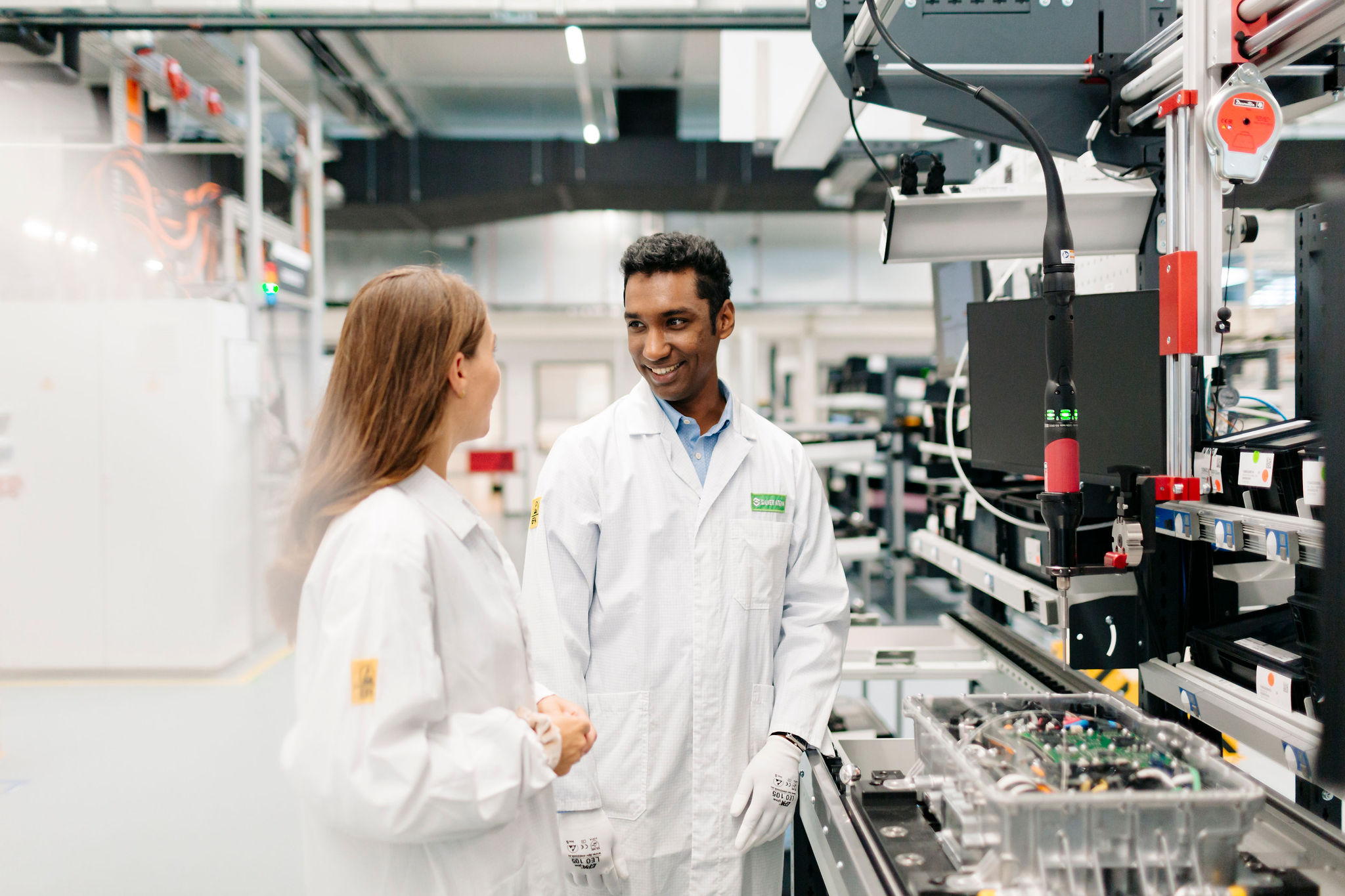 Two Silver Atena employees discussing the production of electronic control units at an automated assembly station.