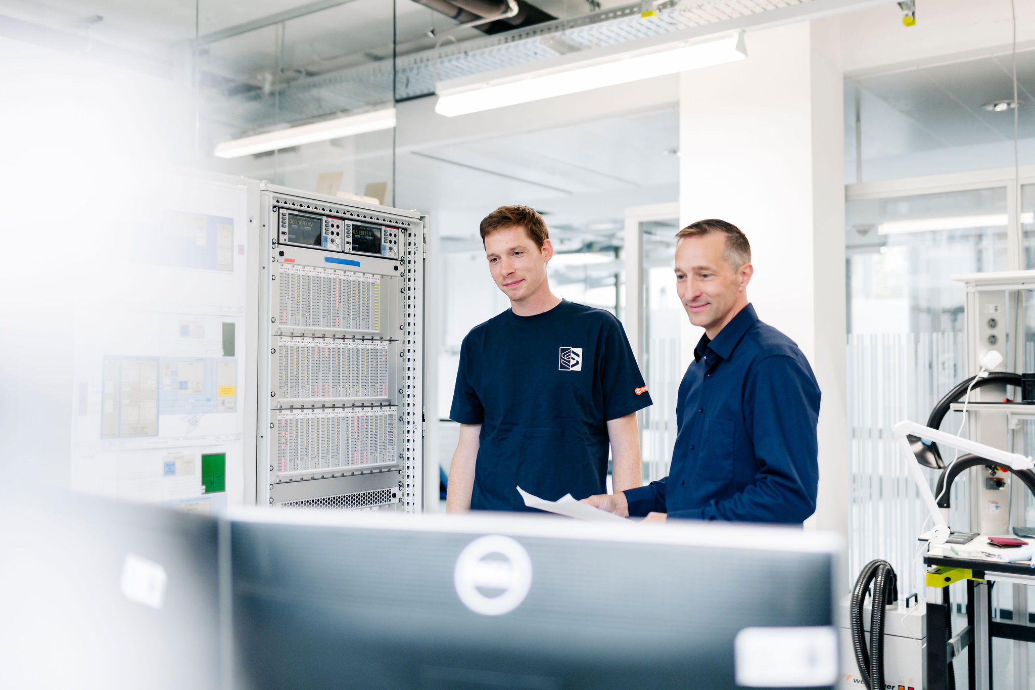 Two Silver Atena employees reviewing technical documentation and measurement data at a modular test bench in the development laboratory.