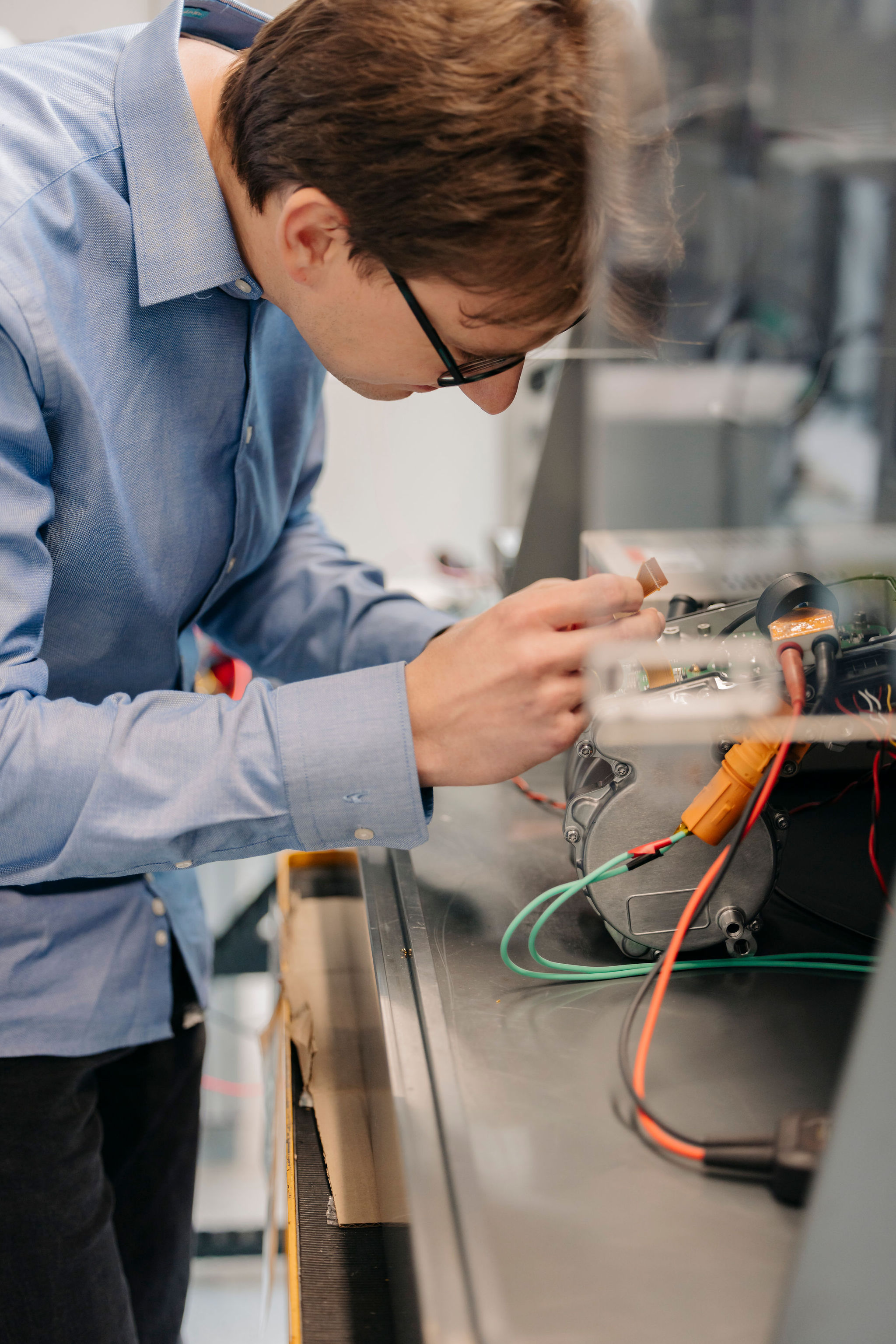 Silver Atena engineer examining an electronic assembly with a metal housing and connected cables in the development laboratory.