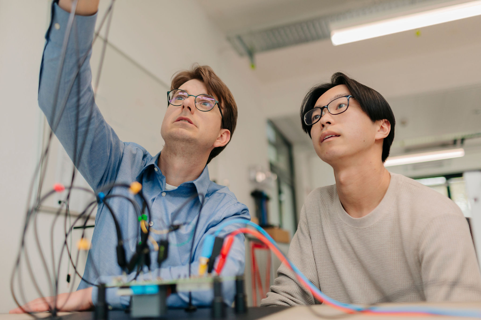 Two engineers analyzing a technical test setup with measurement cables and electronic components in the development laboratory.