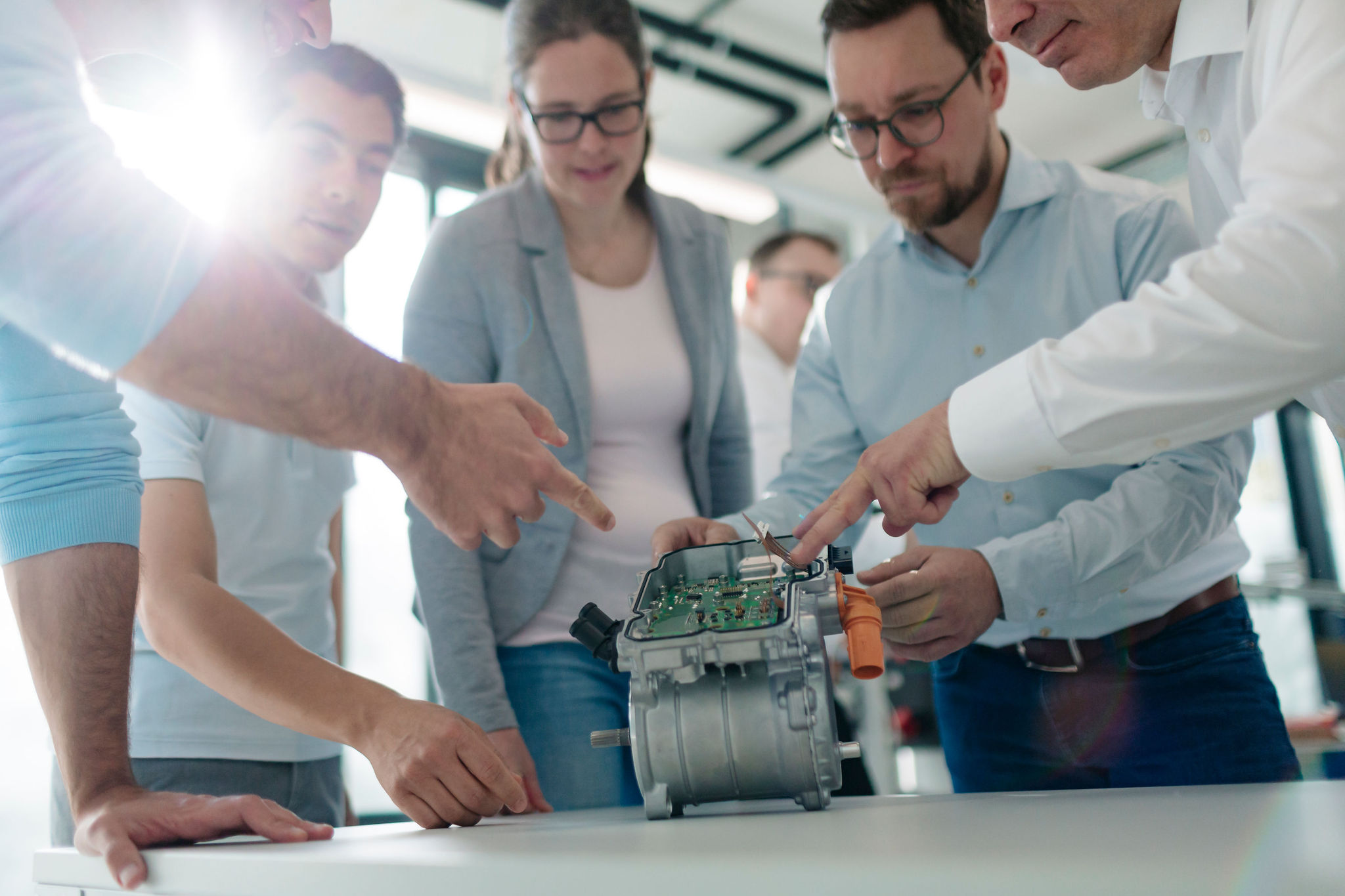 Five Silver Atena employees jointly inspecting an open electronic assembly with a printed circuit board and metal housing.