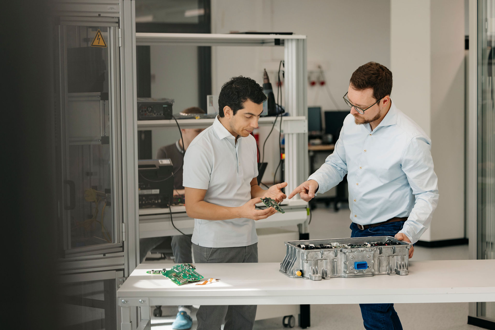 Two Silver Atena engineers discussing a printed circuit board (PCB) and an open control unit housing in the development laboratory.