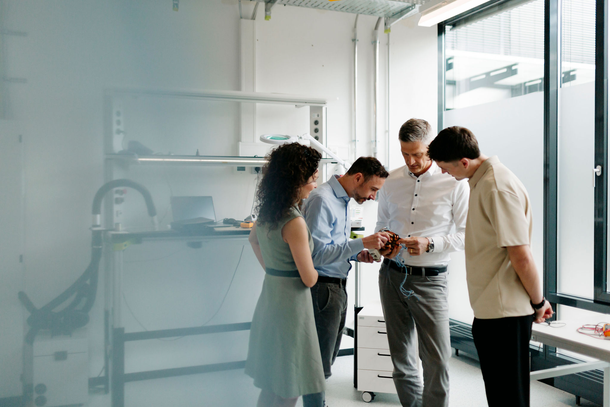 Four Silver Atena employees jointly examining an electronic assembly with connectors in the development laboratory.