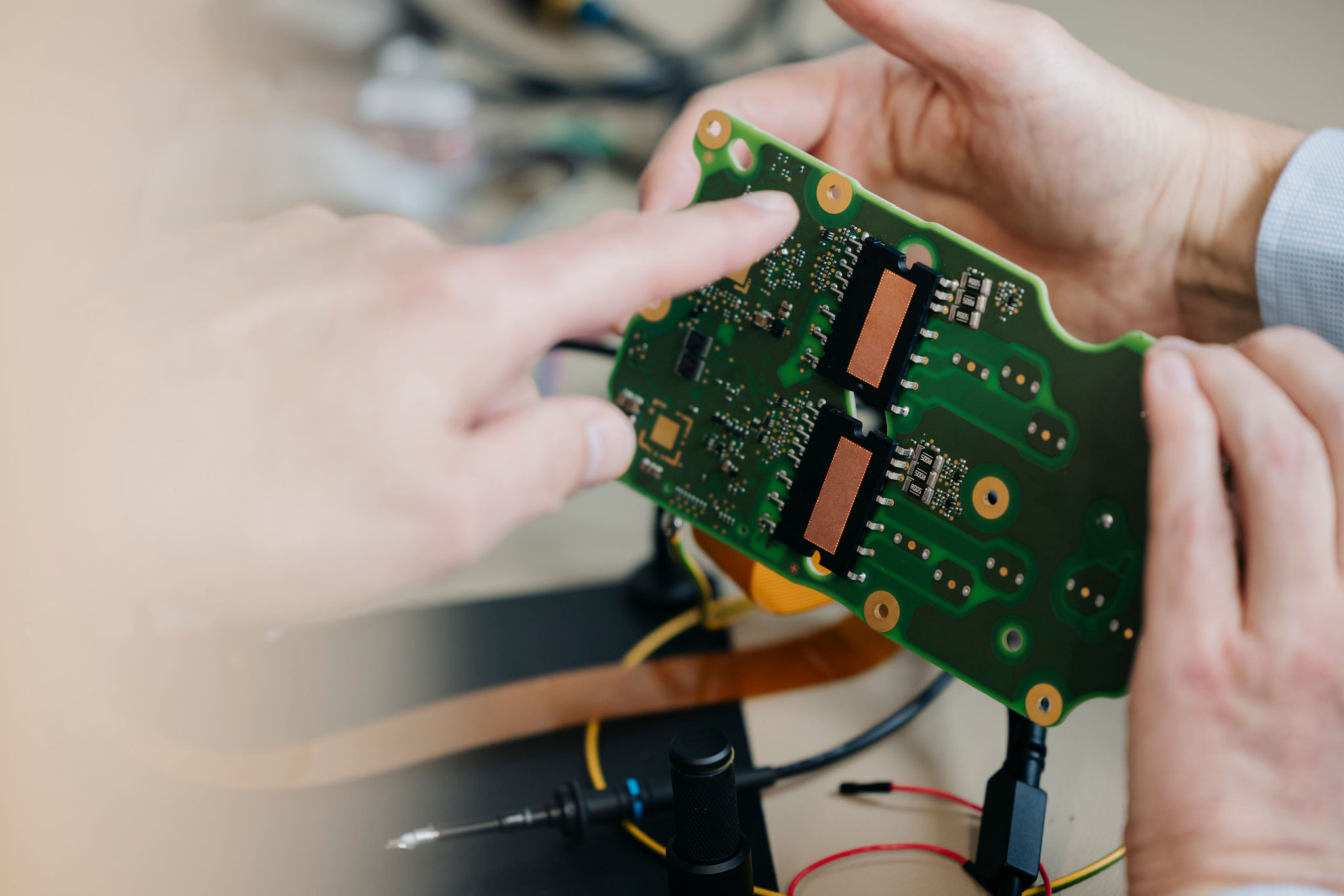 Close-up of an assembled printed circuit board (PCB) with an engineer pointing to electronic components during a technical analysis.