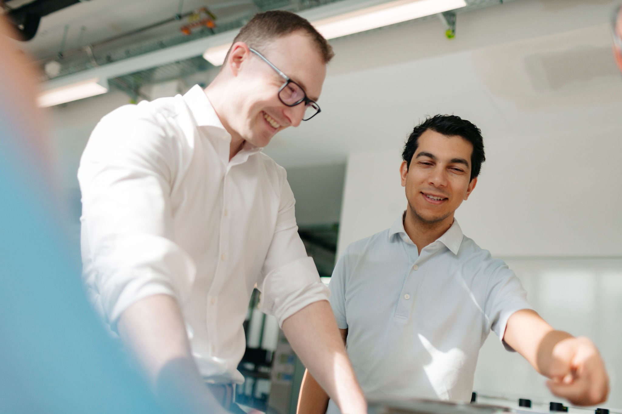 Two Silver Atena employees discussing technical details of an electronic assembly at a laboratory workstation.