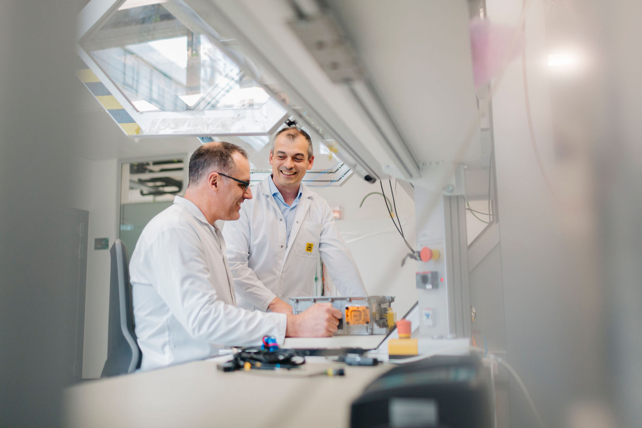 Two Silver Atena engineers discussing the testing of an electronic assembly in a metal housing at a laboratory workstation.