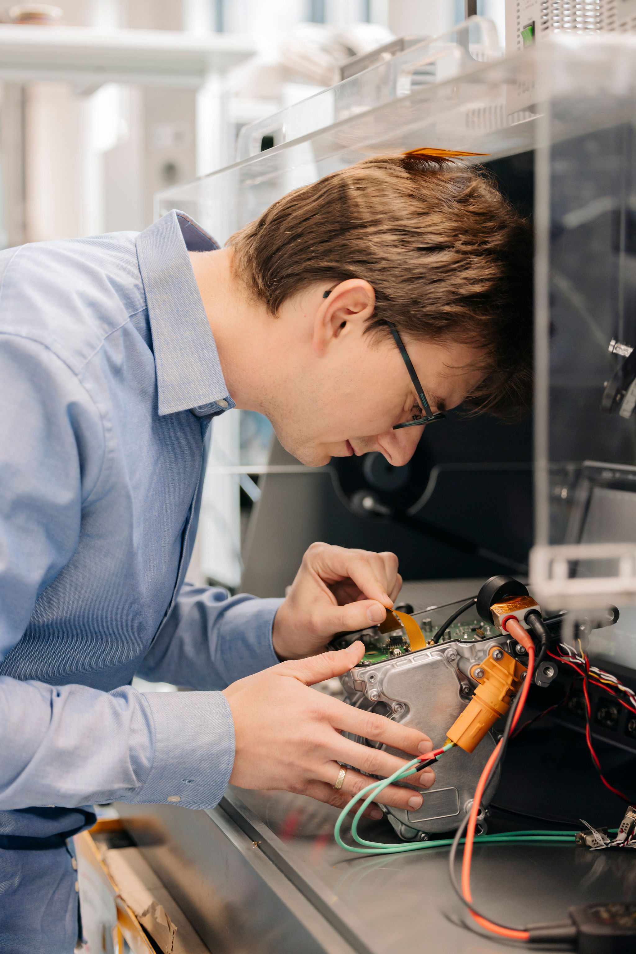 Silver Atena engineer examining an electronic assembly with an open metal housing and connected cables.