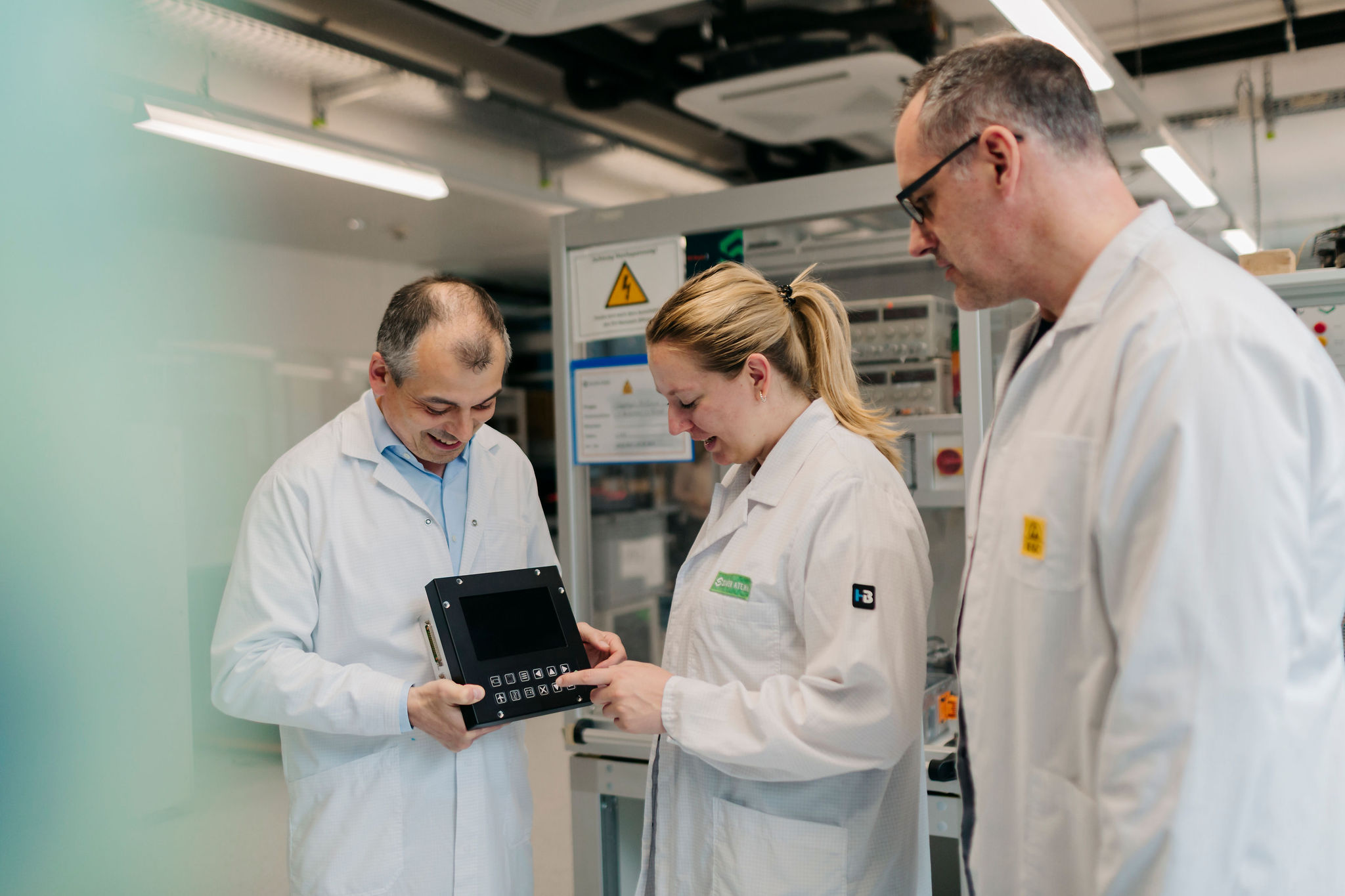 Three Silver Atena employees jointly testing an electronic control and display unit in the development laboratory.