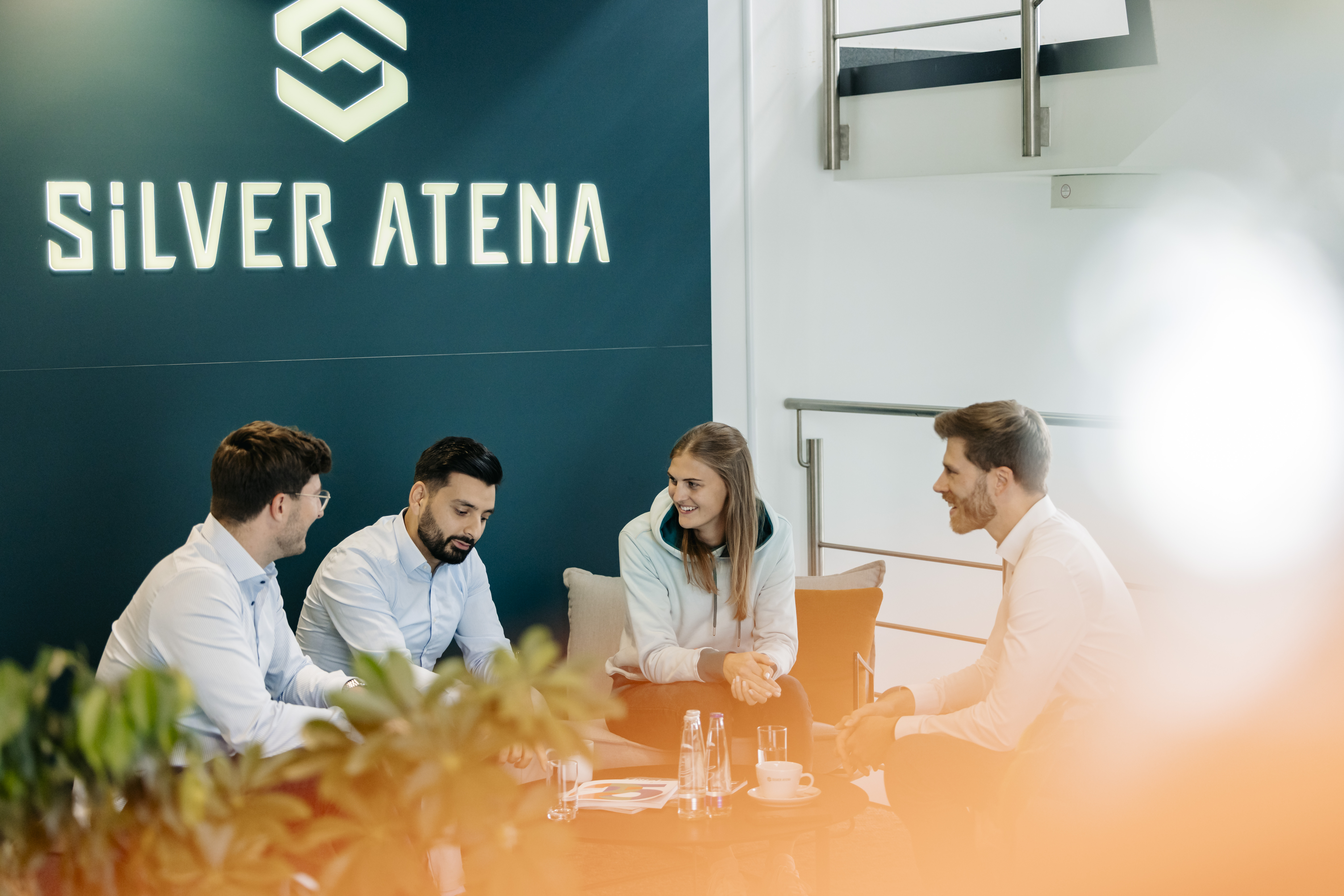 People sit on couch in front of wall with Silver Atena logo.