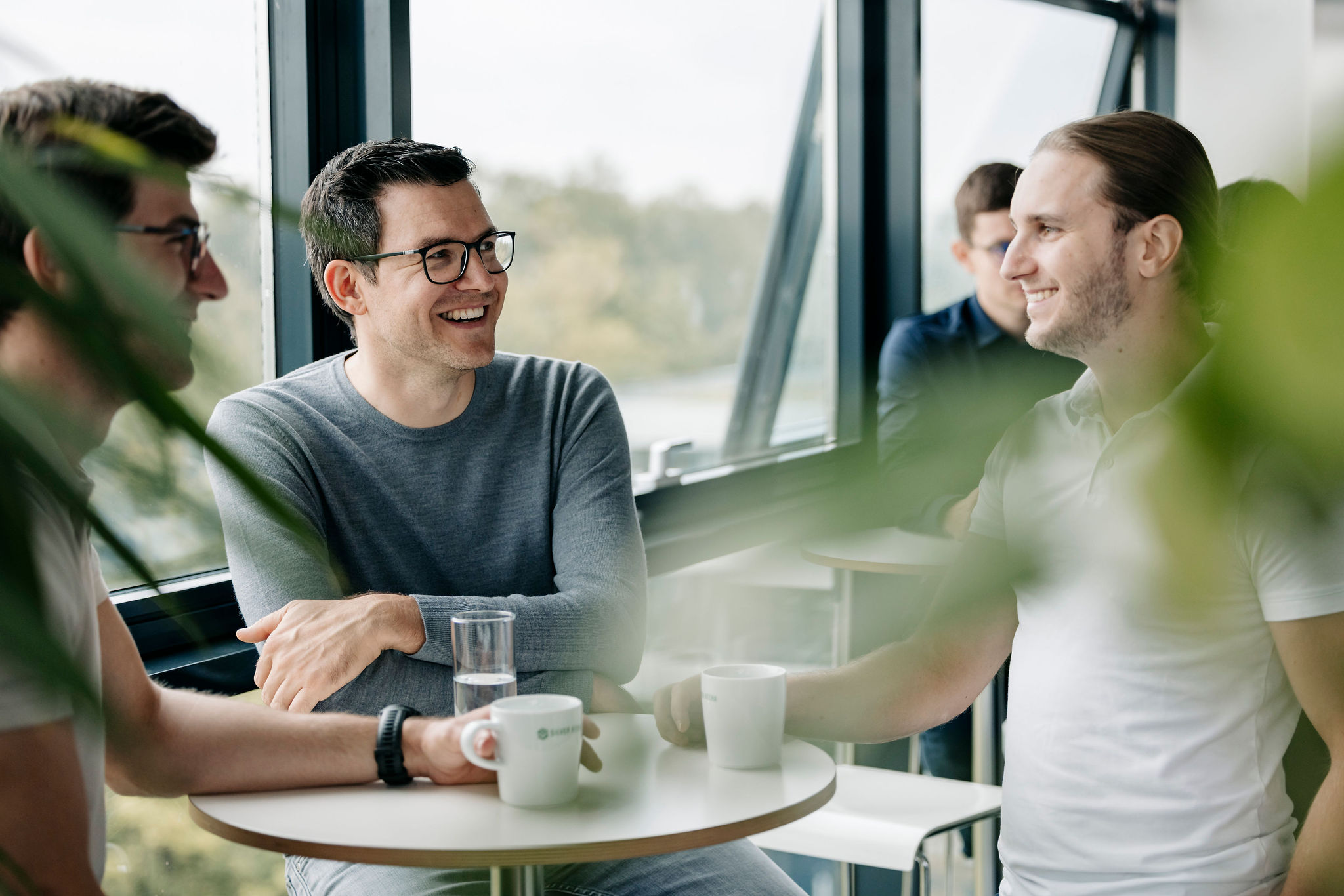 Group at a standing table in a lounge area with windows in the background.